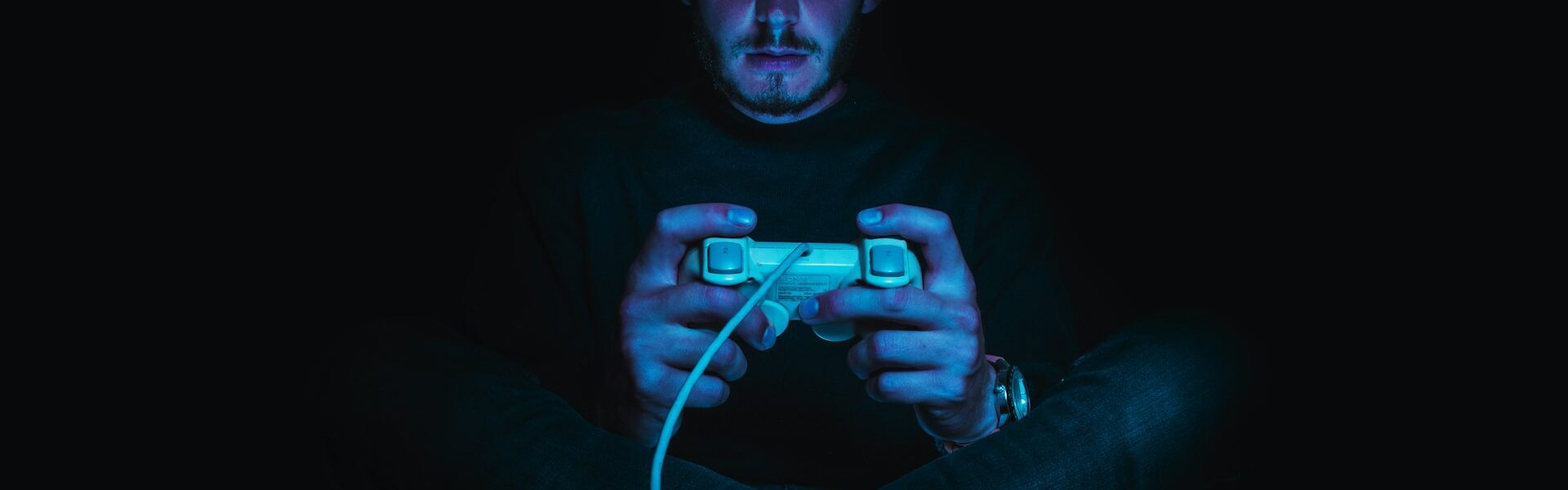 a person sitting in pitch dark with a console controller in his hands, playing Dark Souls after consulting a Dark Souls guide