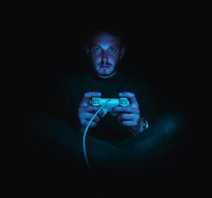 a person sitting in pitch dark with a console controller in his hands, playing Dark Souls after consulting a Dark Souls guide