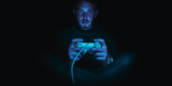 a person sitting in pitch dark with a console controller in his hands, playing Dark Souls after consulting a Dark Souls guide
