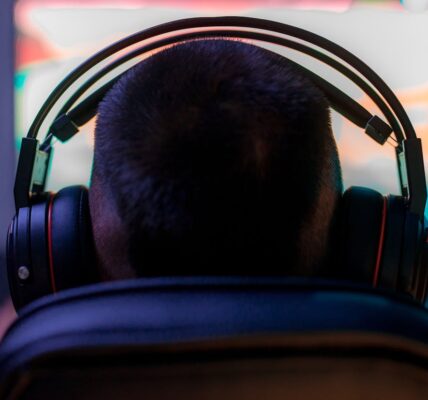 a back view of a person wearing headphones in front of a PC playing Avowed