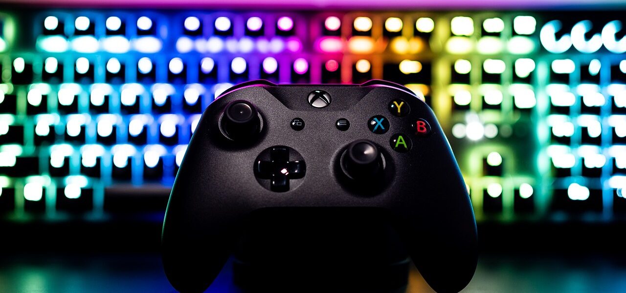a RGB lit keyboard behind a black X Box controller used to play Assassin's Creed Shadows