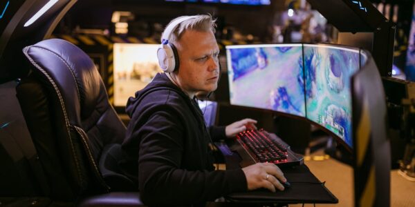 a man playing League of Legends Act 2 on a PC setup with 3 monitors