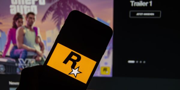 a person holding a phone with the Rockstar logo with GTA VI trailer in the background on a monitor