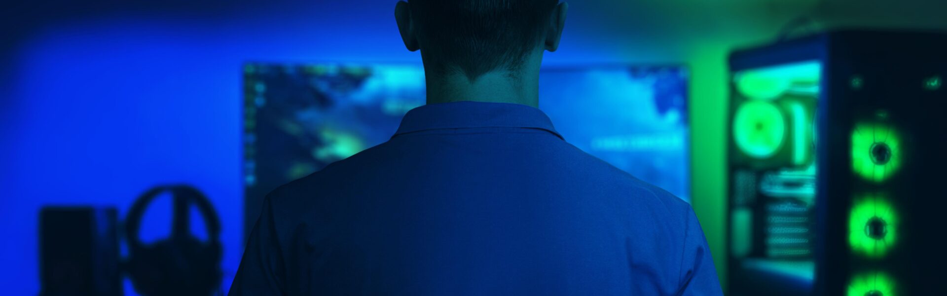 a man sitting in a dark room playing The Precinct on his PC that glows blue and green