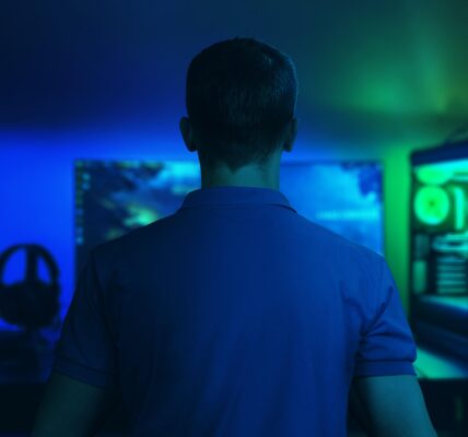 a man sitting in a dark room playing The Precinct on his PC that glows blue and green