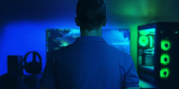 a man sitting in a dark room playing The Precinct on his PC that glows blue and green