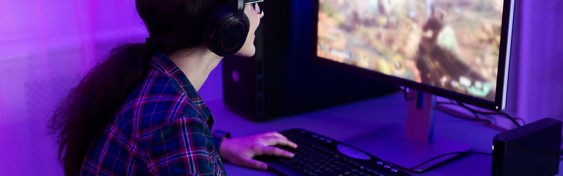 a woman playing Rust on her PC in a purple lit room