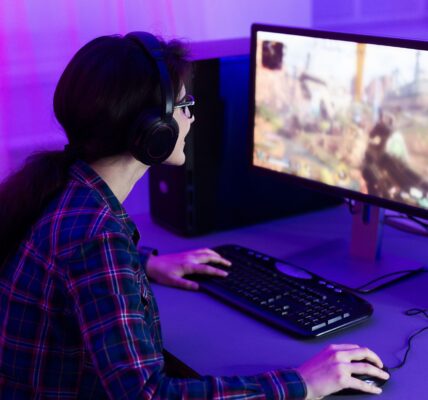 a woman playing Rust on her PC in a purple lit room