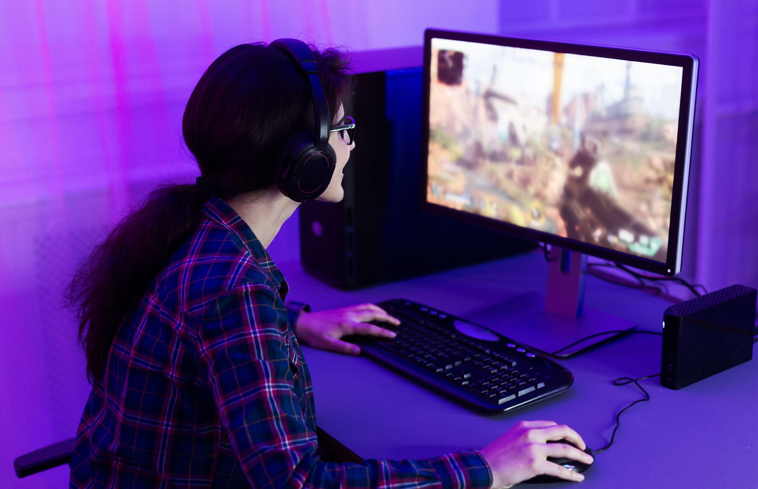 a woman playing Rust on her PC in a purple lit room